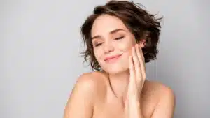 Woman with short hair smiling with eyes closed while gently touching her cheek