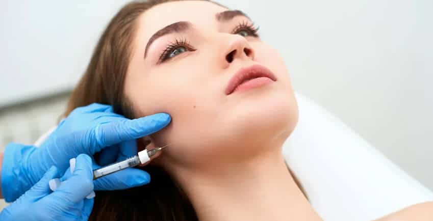 Medical professional administering a dermal filler injection to a patient's cheek during a facial rejuvenation treatment.